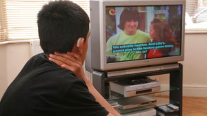 A hard of hearing boy with a hearing aid watches TV with the help of the RNID loop system. From the Solutions Catalogue 2008.